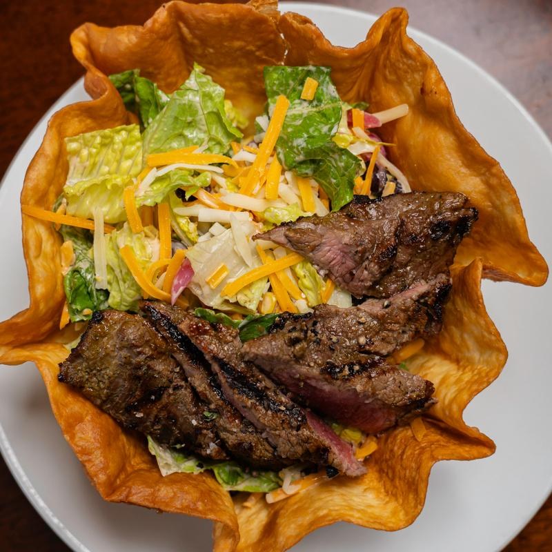 A taco salad in a crispy tortilla bowl topped with sliced steak at Amici Tavern in North Haven