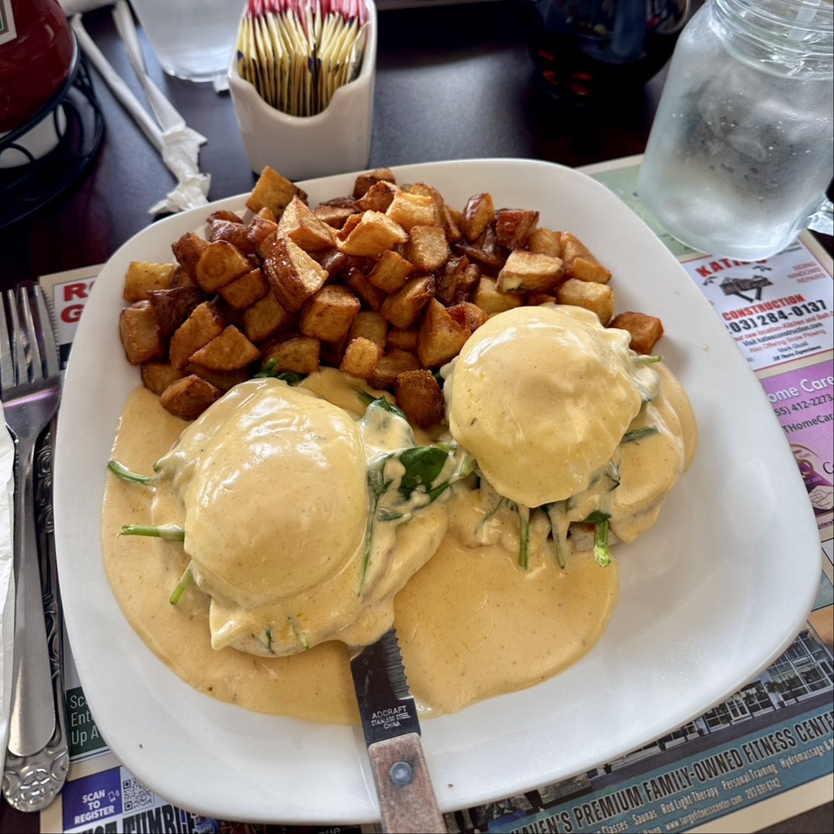 Eggs Benedict covered in hollandaise next to a pile of crispy home fries at Crazy Toast House