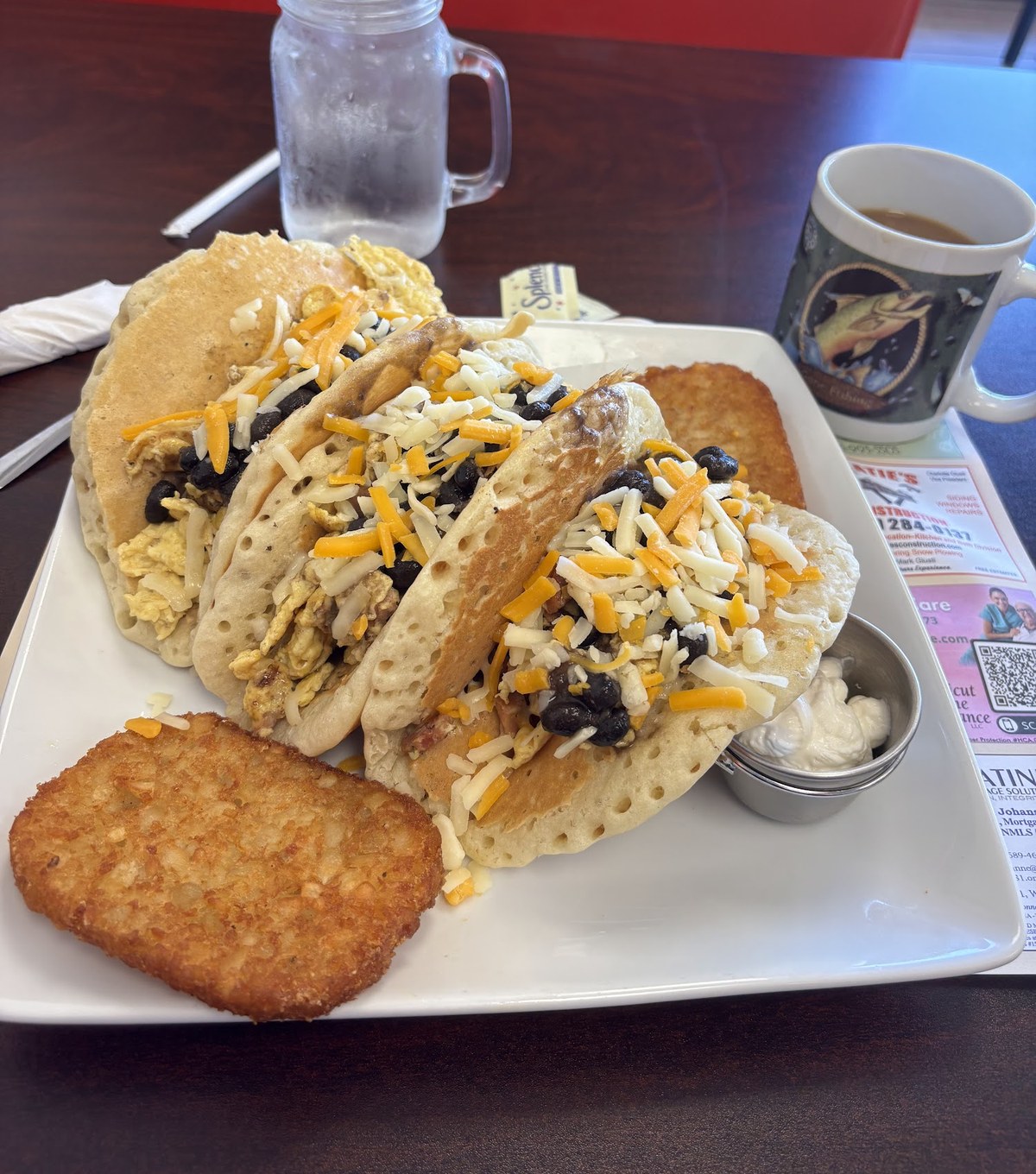 Three pancake-shell breakfast tacos topped with shredded cheese, with a hash brown patty on the plate