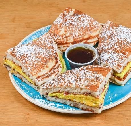Wedges of stuffed pancake quesadilla filled with eggs and cheese, dusted with powdered sugar around a cup of syrup