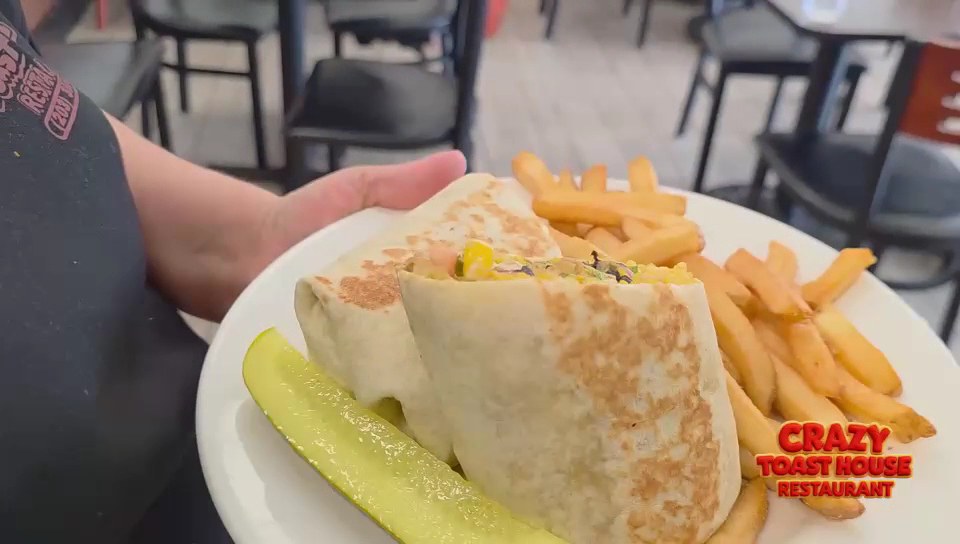 A Crazy Toast House wrap cut in half with French fries and a pickle spear on a white plate