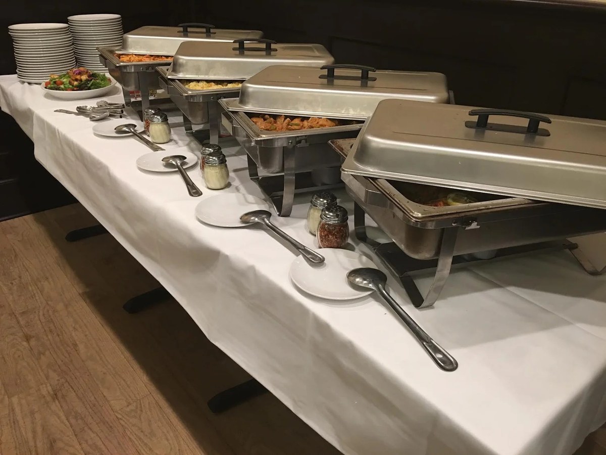Catering chafing trays lined up on a white tablecloth at J Roo’s