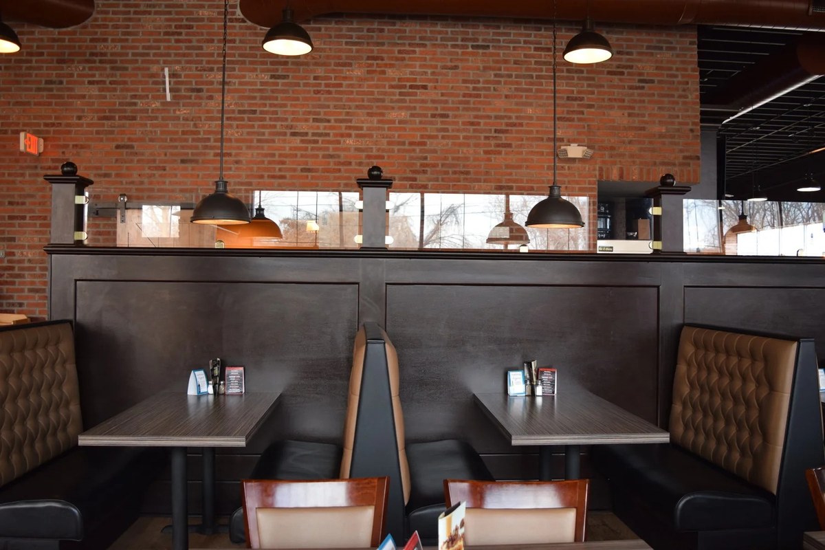 Black booths and tables under pendant lights in front of a brick wall in the J Roo’s dining room