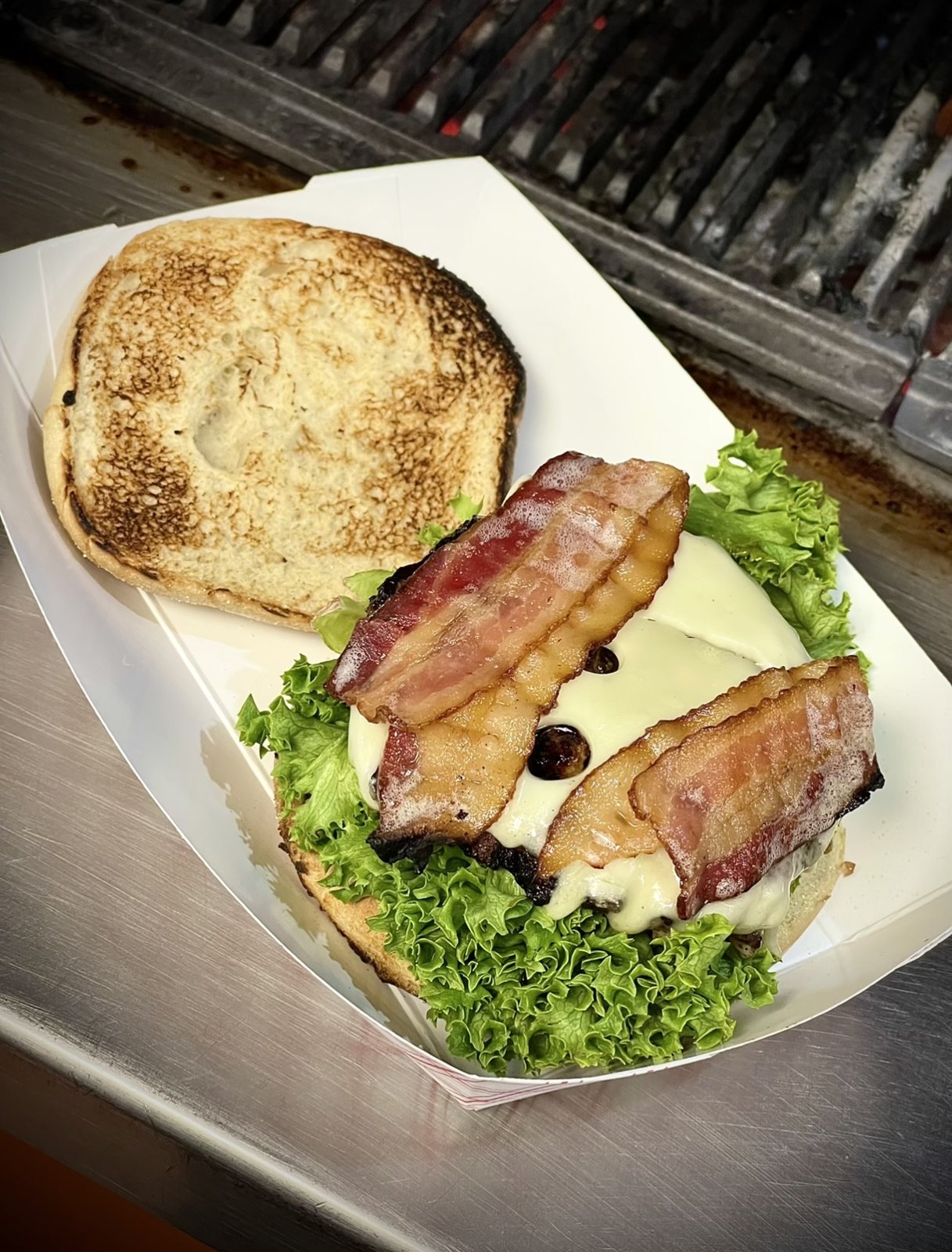 A bacon burger with lettuce at Nick’s Char Pit, beside the char grill