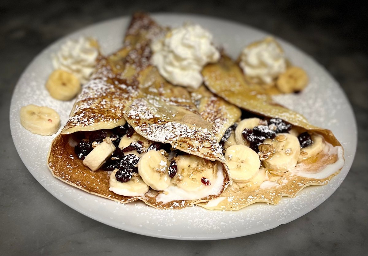 Sam's Crêpe with bananas, yogurt, granola and whipped cream on a white plate