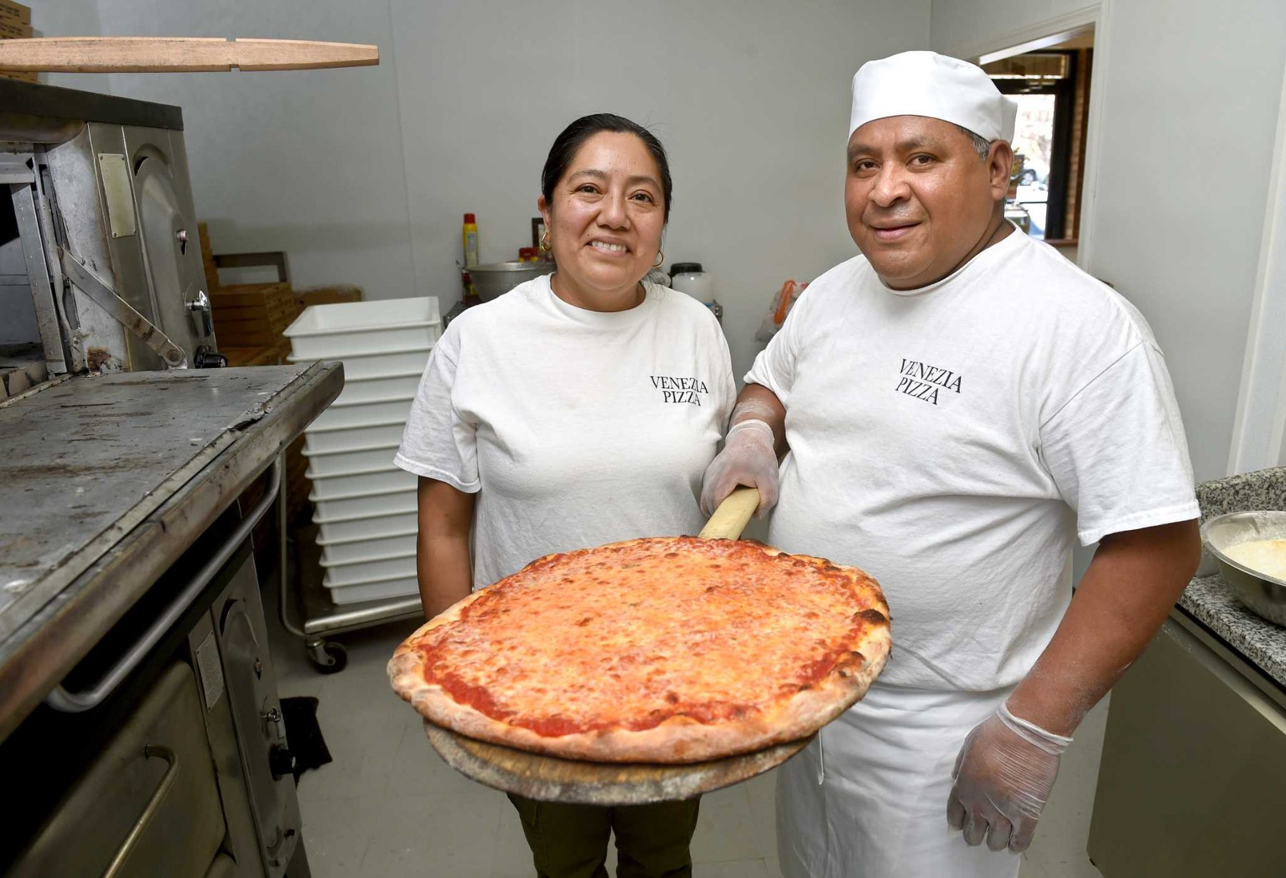 Two Venezia Pizza cooks in the kitchen holding a fresh cheese pie
