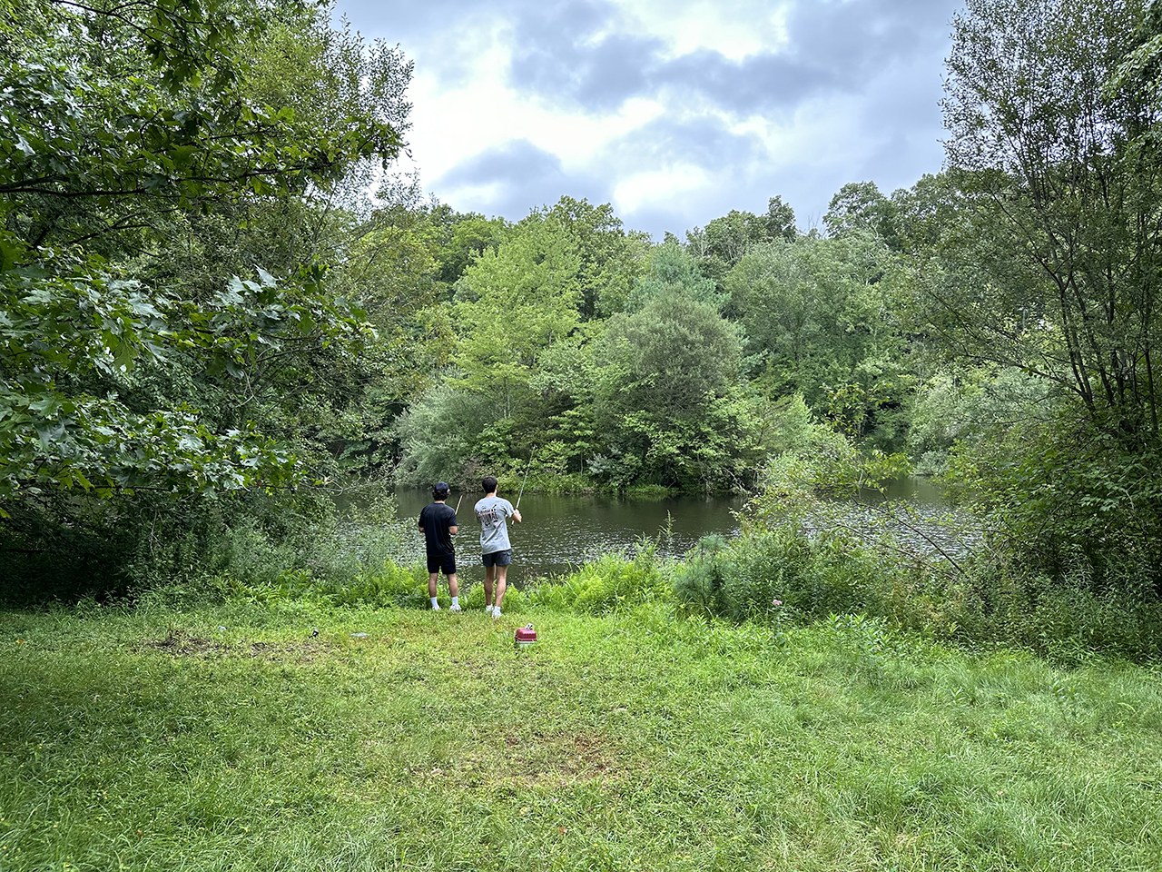 Two visitors stand at the edge of the pond beyond a grassy clearing at Wah Wah Taysee